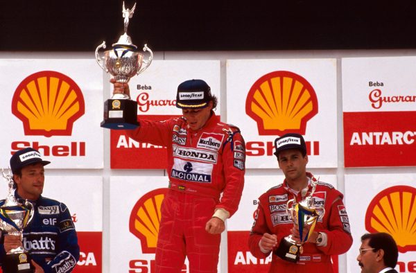 Met pijn en moeite tilt Ayrton Senna de beker op, nadat hij voor het eerst zijn thuisrace heeft gewonnen.