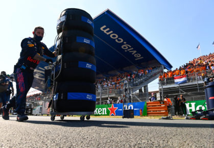 Een lid van Red Bull loopt met banden en bandenwarmers over de grid.